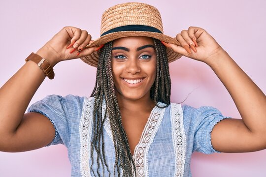 Young african american woman with braids wearing summer hat smiling with a happy and cool smile on face. showing teeth.