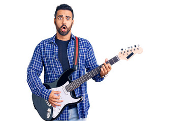 Young hispanic man playing electric guitar scared and amazed with open mouth for surprise, disbelief face