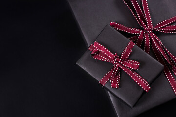 Two gift boxes wrapped in black paper with a red ribbon on a dark background with copy space. Black Friday banner