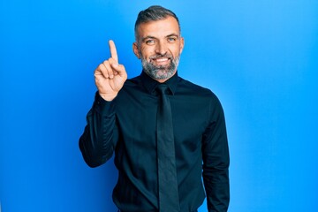 Middle age handsome man wearing business shirt and tie showing and pointing up with finger number one while smiling confident and happy.