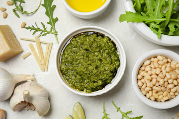 Bowl of tasty arugula pesto and ingredients on light table, flat lay