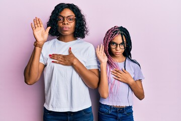 Beautiful african american mother and daughter wearing casual clothes and glasses swearing with...