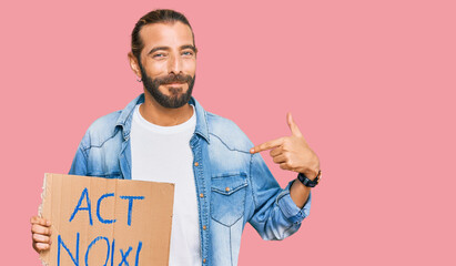 Attractive man with long hair and beard holding act now banner pointing finger to one self smiling...