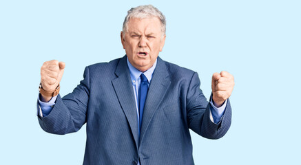 Senior grey-haired man wearing business jacket angry and mad raising fists frustrated and furious while shouting with anger. rage and aggressive concept.