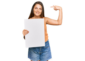 Young caucasian woman holding blank empty banner pointing finger to one self smiling happy and proud