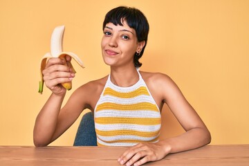 Brunette teenager girl eating banana as healthy snack thinking attitude and sober expression looking self confident