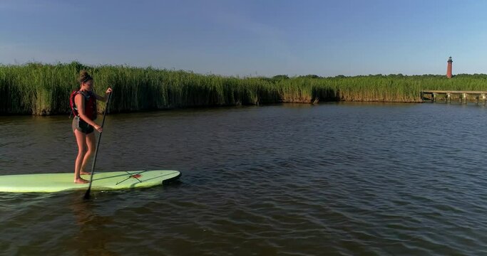 Attractive female on a stand up paddleboard in the Currituck sound in the Outer Banks with a lighthouse in the background