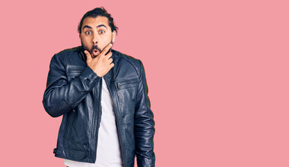 Fototapeta premium Young arab man wearing casual leather jacket looking fascinated with disbelief, surprise and amazed expression with hands on chin