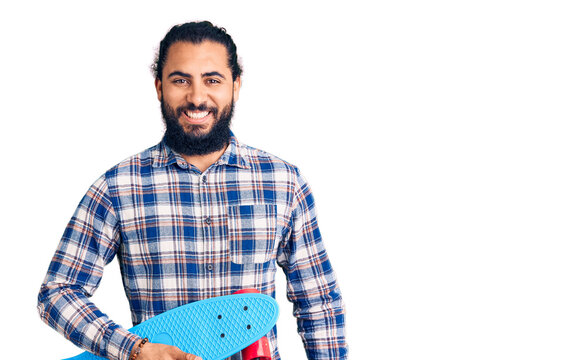 Young arab man holding skate looking positive and happy standing and smiling with a confident smile showing teeth