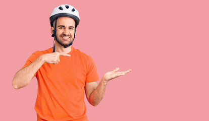 Young handsome man wearing bike helmet amazed and smiling to the camera while presenting with hand and pointing with finger.