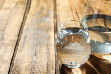 Glass and jug of water on wooden table, space for text. Refreshing drink