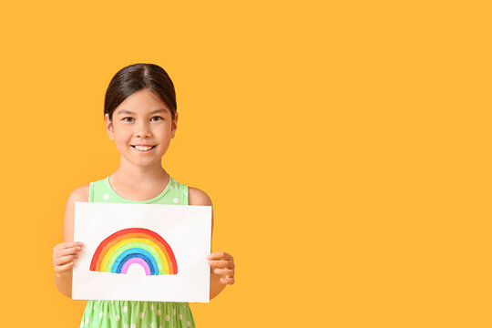 Little girl with painting of rainbow on paper sheet against color background