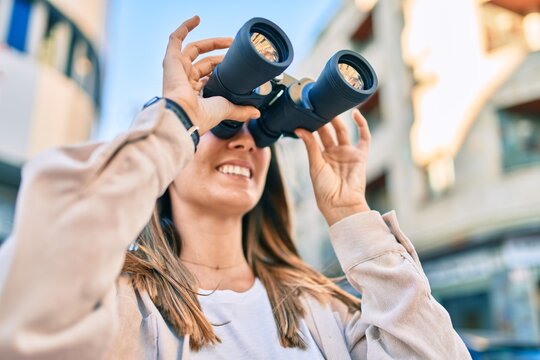 Young caucasian woman smiling happy looking for new opportunity using binoculars walking at the city.