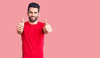 Young handsome man with beard wearing casual t-shirt approving doing positive gesture with hand, thumbs up smiling and happy for success. winner gesture.