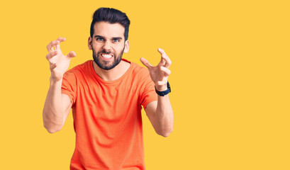 Young handsome man with beard wearing casual t-shirt shouting frustrated with rage, hands trying to strangle, yelling mad