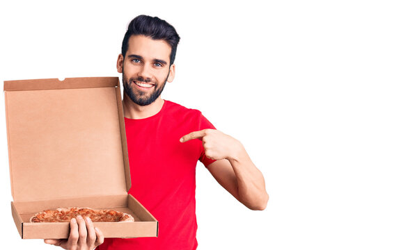 Young handsome man with beard holding delivery cardboard with italian pizza pointing finger to one self smiling happy and proud