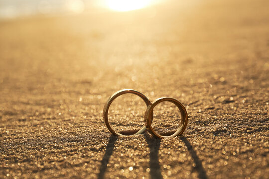 Gold wedding rings on sandy beach at sunset, closeup