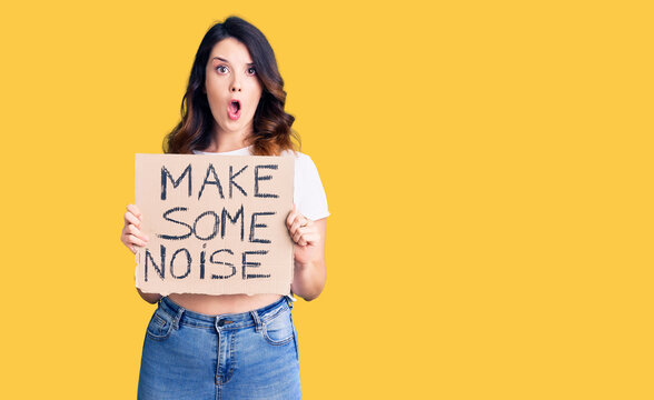 Beautiful young brunette woman holding make some noise banner scared and amazed with open mouth for surprise, disbelief face