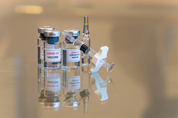 A set of three COVID-19 vaccination drug dose trial vials with a filled injection syringe in the front - 013