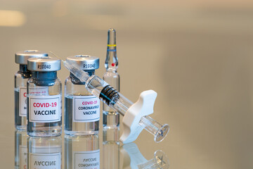 Closeup view of a set of three COVID-19 vaccination drug dose trial vials with a filled injection syringe in the front - 015