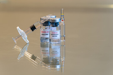 A set of COVID-19 vaccination drug dose trial vials with a filled injection syringe in the front with a tiny droplet escaping from the needle tip with copy space - 041
