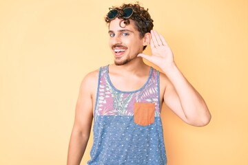 Young caucasian man with curly hair wearing casual style with sleeveless shirt smiling with hand over ear listening and hearing to rumor or gossip. deafness concept.