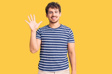 Young handsome man with curly hair wearing casual clothes showing and pointing up with fingers number five while smiling confident and happy.