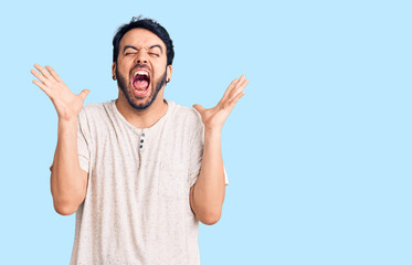 Naklejka premium Young hispanic man wearing casual clothes celebrating mad and crazy for success with arms raised and closed eyes screaming excited. winner concept