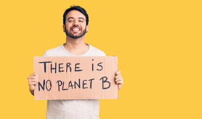 Young hispanic man holding there is no planet b banner looking positive and happy standing and...