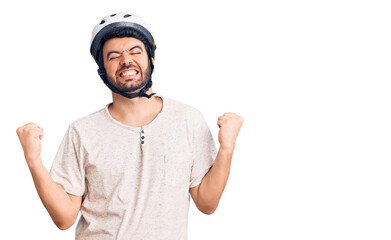 Young hispanic man wearing bike helmet very happy and excited doing winner gesture with arms raised, smiling and screaming for success. celebration concept.