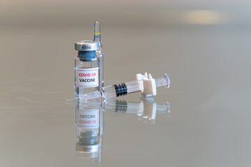 A closeup vial of COVID-19 Coronvavirus vaccine with a syringe on the right and needle tip in the front - 093