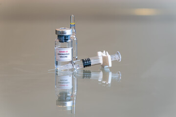 A closeup vial of COVID-19 Coronvavirus vaccine with a syringe on the right and needle tip in the front - 100