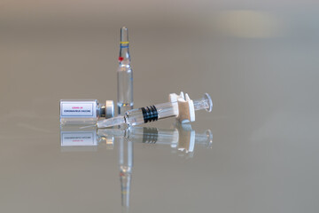 A sideways mini vial of COVID-19 Coronvavirus vaccine with a syringe on the right and an ampule in the rear - 131