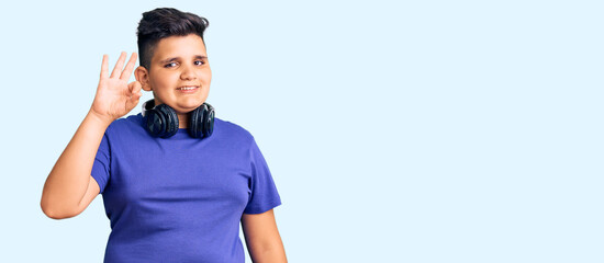 Little boy kid listening to music wearing headphones smiling positive doing ok sign with hand and fingers. successful expression.