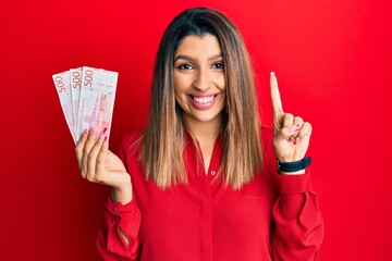 Beautiful brunette woman holding 500 swedish krona banknotes smiling with an idea or question...