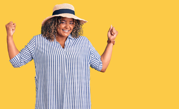 Young african american plus size woman wearing summer hat showing arms muscles smiling proud. fitness concept.