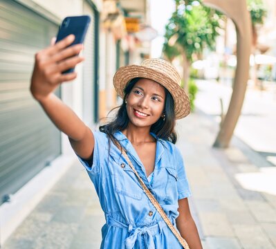 Young beautiful indian woman wearing summer hat smiling happy making selfie by the smartphone at the city.
