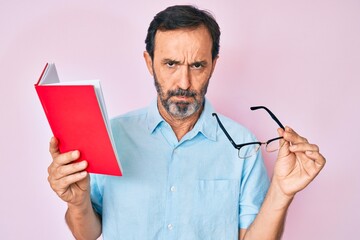 Middle age hispanic man reading book holding glasses skeptic and nervous, frowning upset because of...