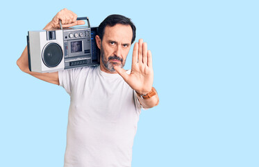 Middle age handsome man listening to music using vintage boombox with open hand doing stop sign with serious and confident expression, defense gesture