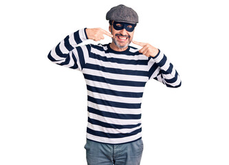 Middle age handsome man wearing burglar mask smiling cheerful showing and pointing with fingers teeth and mouth. dental health concept.