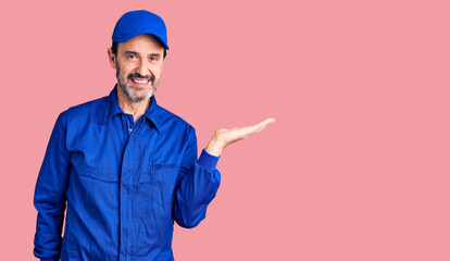 Middle age handsome man wearing mechanic uniform smiling cheerful presenting and pointing with palm of hand looking at the camera.