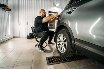 Fototapeta na wymiar Car detailing. Worker prepares rear lights of SUV for polishing in garage.