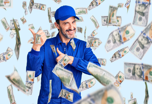 Middle age handsome man wearing mechanic uniform pointing to the back behind with hand and thumbs up, smiling confident