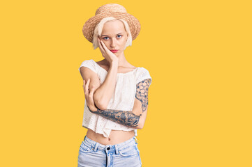 Young blonde woman with tattoo wearing summer hat thinking looking tired and bored with depression...