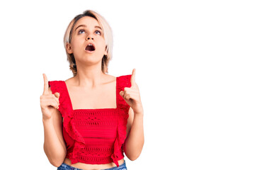 Young beautiful blonde woman wearing casual clothes amazed and surprised looking up and pointing with fingers and raised arms.
