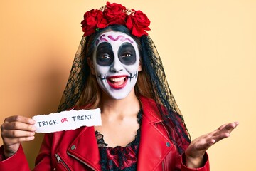 Woman wearing day of the dead costume holding trick or treat paper celebrating achievement with happy smile and winner expression with raised hand