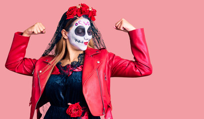 Woman wearing day of the dead costume over background showing arms muscles smiling proud. fitness concept.
