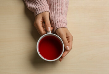 Woman holding cup of tea at wooden table, top view