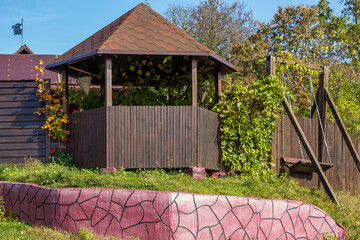 Cozy gazebo and swing made of wood in the garden, the fence of the summer cottage
