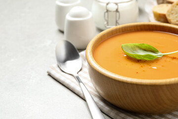Tasty creamy pumpkin soup with basil in bowl on grey table. Space for text